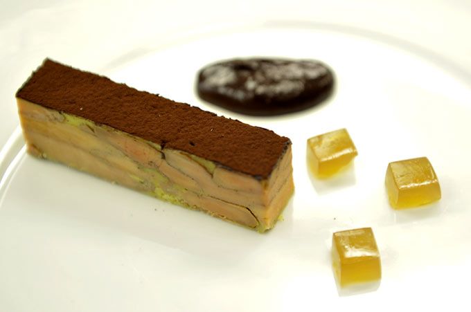 Postre en plato blanco: pastel de capas con chocolate, acompañado de tres cubos de dulce y una pequeña porción de chocolate.
