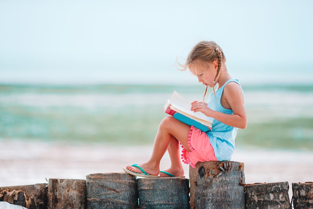 Niña pequeña leyendo un libro con el mar al fondo