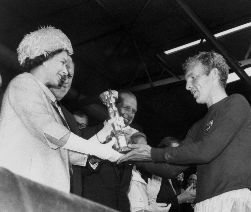La reina Isabel II presentando el Trofeo Oficial de la Copa del Mundial al capitán de la Selección de Inglaterra Bobby Moore, mientras el Duque de Edimburgo sonríe al fondo. La fotografía fue tomada en el Wembley Stadium en Londres, el 30 de julio de 1966.