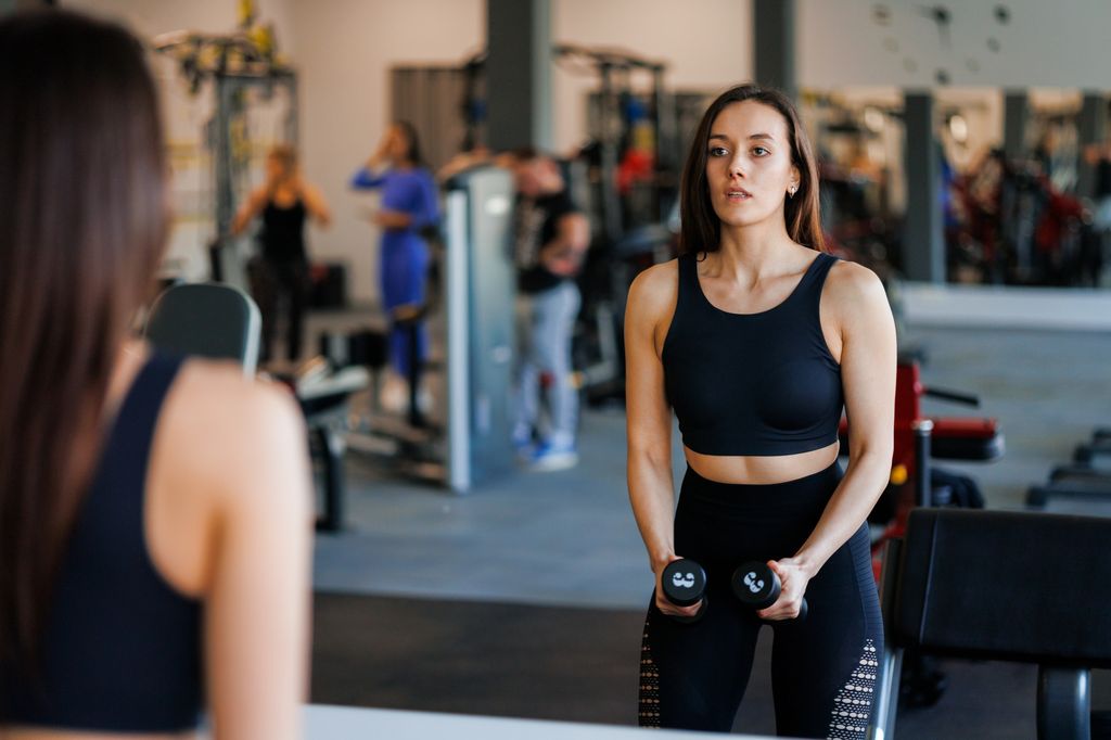Una mujer en el gimnasio haciendo un remo con mancuernas