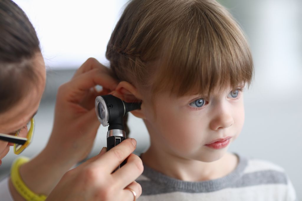 Niña en la consulta del otorrino mientras la explora con el otoscopio por otitis