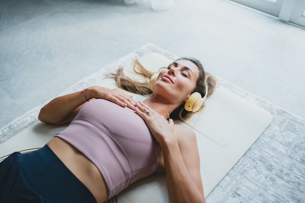 Mujer haciendo la postura de savasana con auriculares