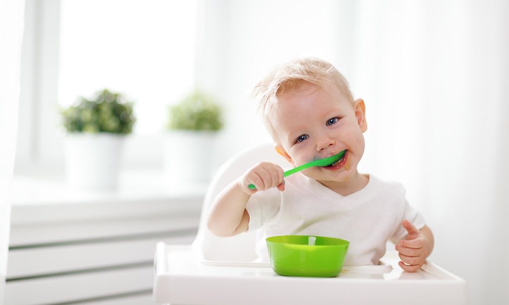 ni o con cuchara en la boca comiendo de plato de comida en su trona