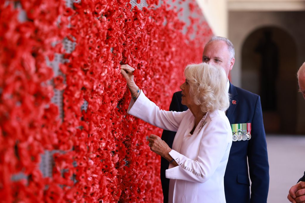 Plano medio de la reina Camilla en su visita a Australia colocando una amapola en un muro