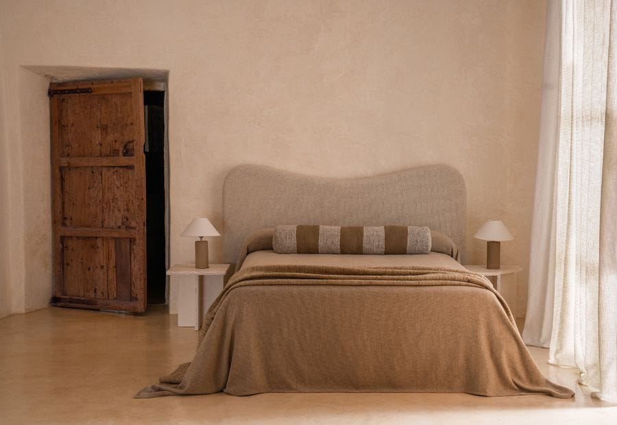 Dormitorio en colores cálidos y neutros y con el cabecero tapizado y de formas sinuosas