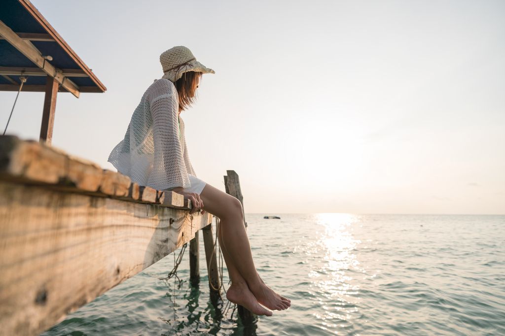 mujer sentada en el muelle mirando al horizonte del mar