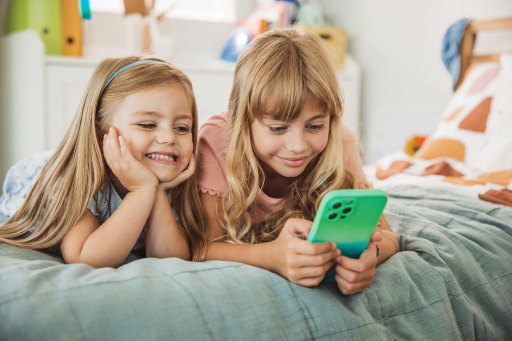 dos niñas usando el teléfono móvil, tumbadas en la cama