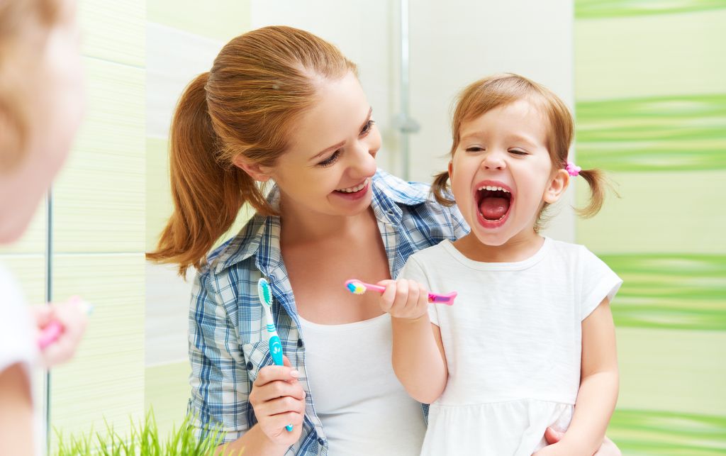 Madre e hija lavándose los dientes felices