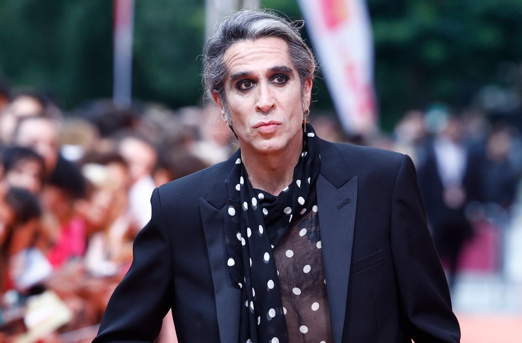 Mario Vaquerizo en traje negro con pañuelo de lunares, caminando entre público.