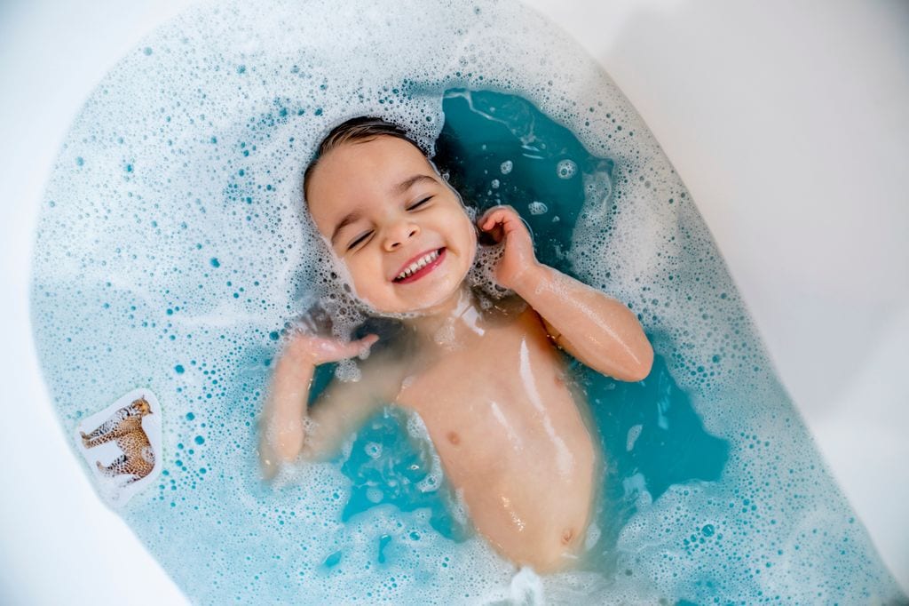 Niño pequeño bañándose en la bañera con el agua azul