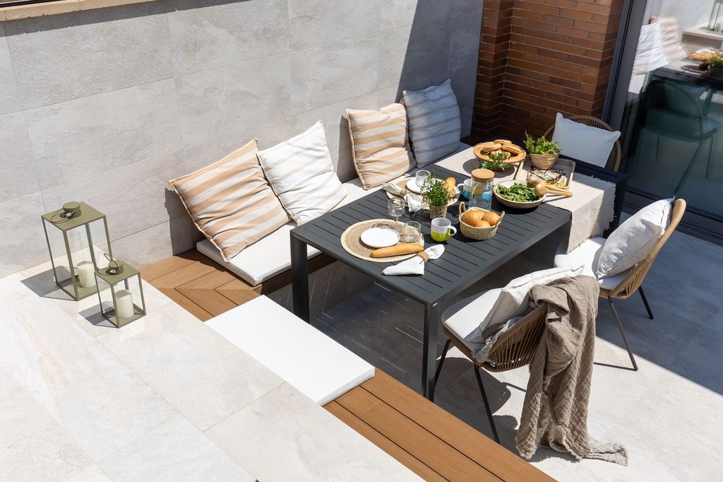 Comedor exterior con mesa negra, banco y sillas. 