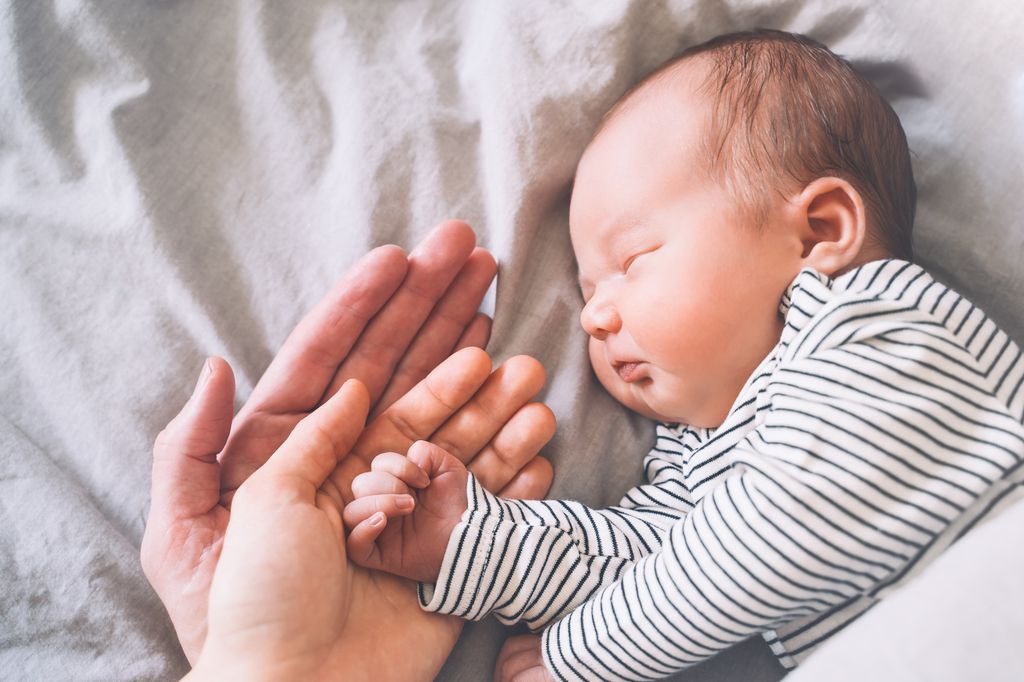 Padre y madre sosteniendo la mano del bebé.