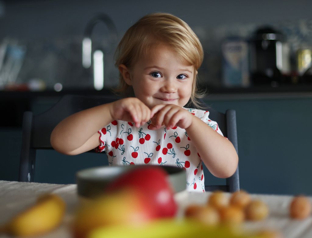 Niña pequeña sentada a la mesa para comer