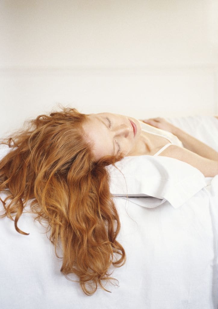 Mujer pelo pelirrojo durmiendo cama blanca