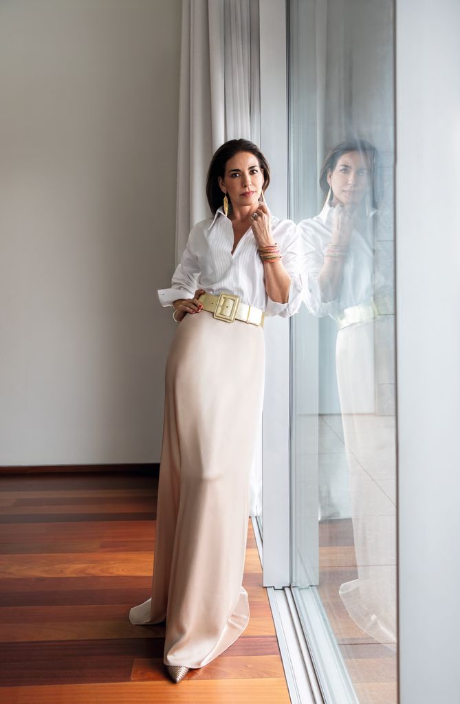 Mariló Montero  con cabello oscuro, camisa blanca y falda beige frente a un espejo.