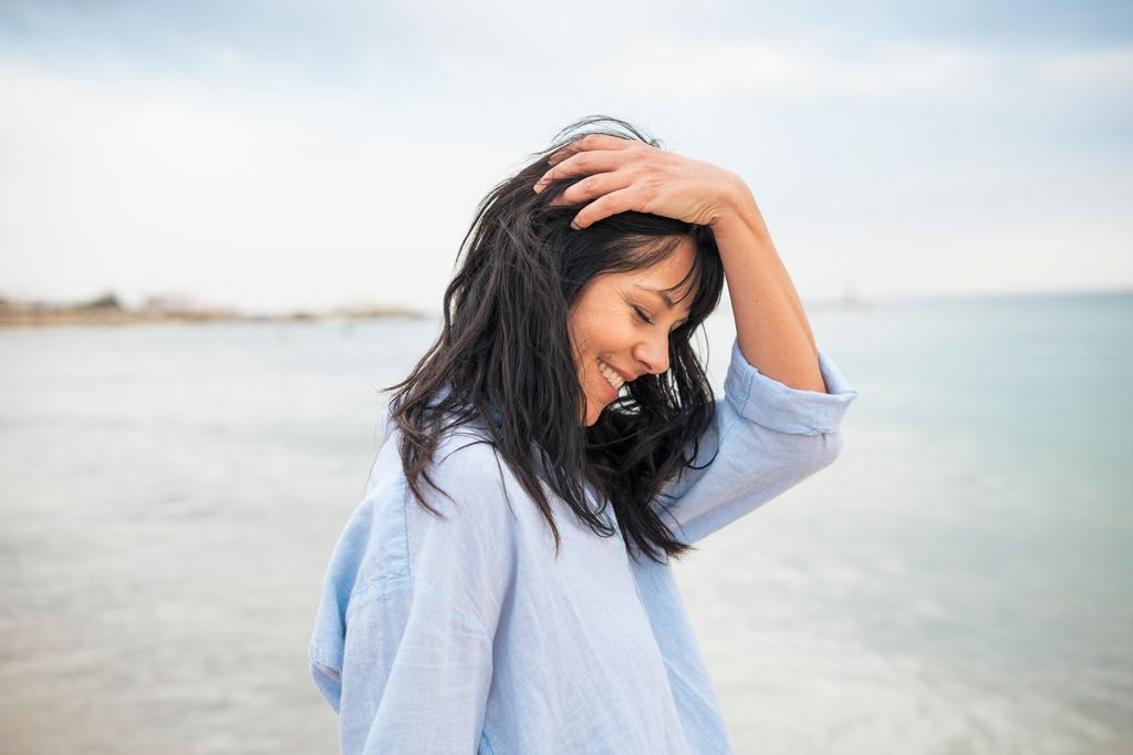 mujer sonriente tocando su cabello en la playa