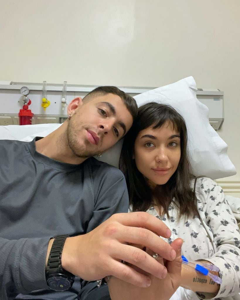 Plano medio de María Becerra y su novio, J Rei, acompañándola en una camilla de hospital