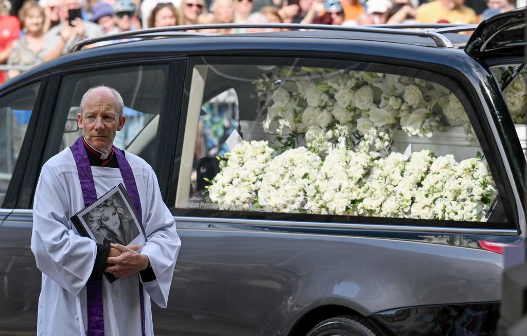 El reverendo Justin Davies sostiene una fotografía de Bonnie Tyler mientras el coche fúnebre, repleto de flores blancas, llega a Swansea Minster para el último adiós a la cantante galesa