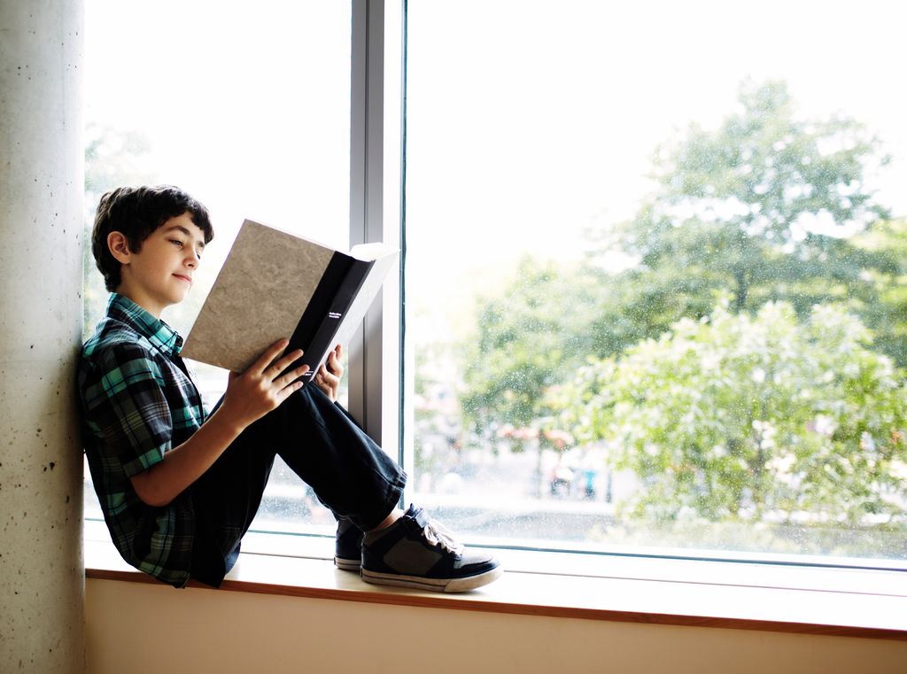 Niño leyendo un libro en una ventana