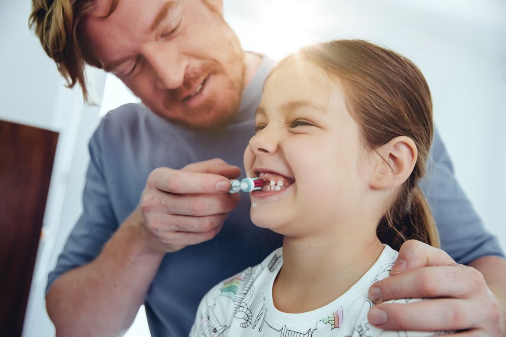 Padre cepillando los dientes a su hija pequeña