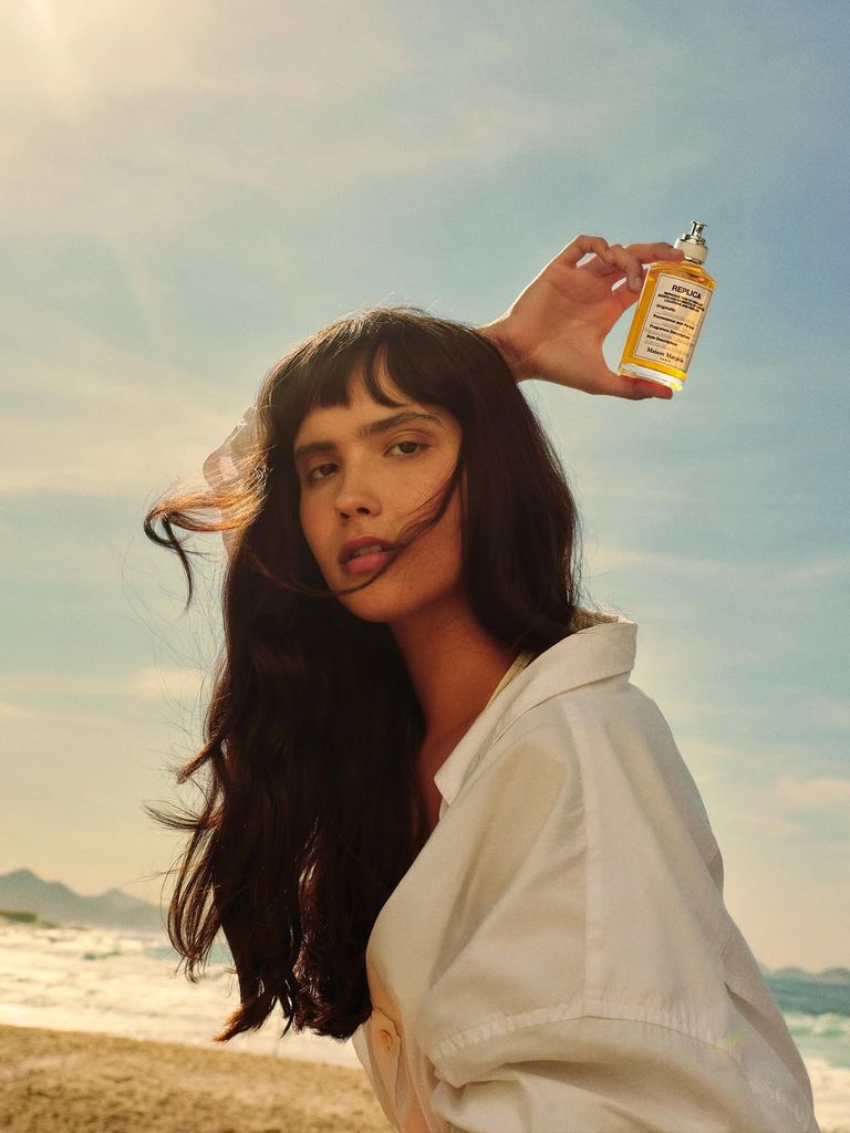 Modelo sosteniendo un frasco de perfume Replica de Maison Margiela en la playa