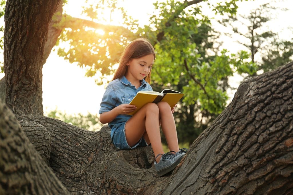 Niña leyendo subida a un árbol