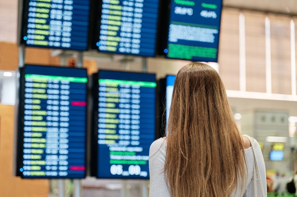 Mujer en el aeropuerto comprobando los paneles de salidas para viajar en avión