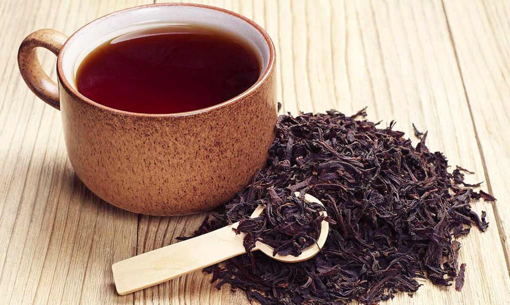 Taza de té negro junto a hojas de la planta