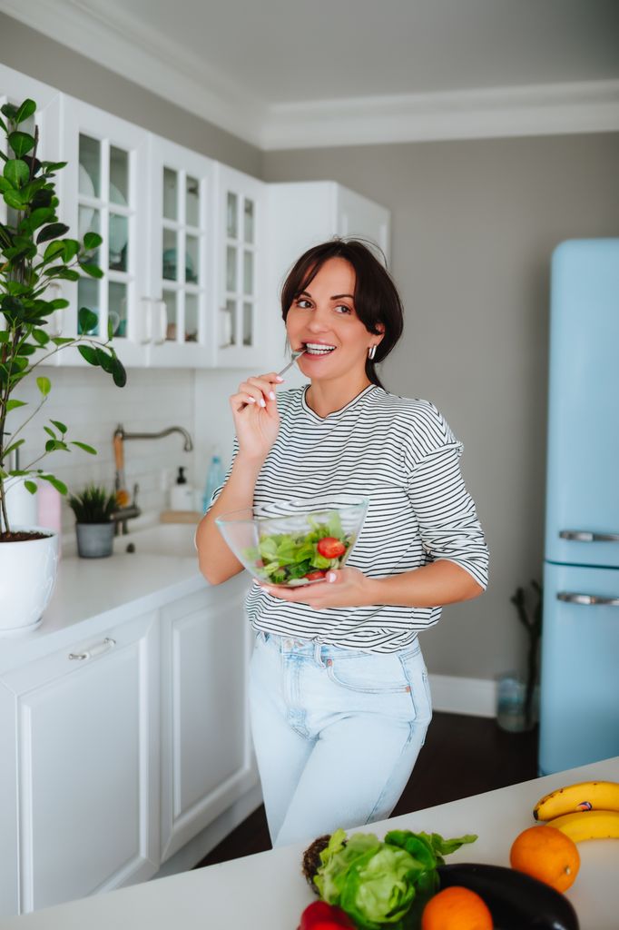 Mujer comiendo apio y ensalada en la cocina