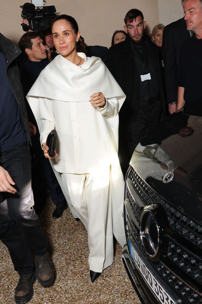 Meghan Markle optó por un sofisticado look firmado por Balenciaga: una capa blanca sobre una camisa de seda abotonada y pantalón amplio color crema