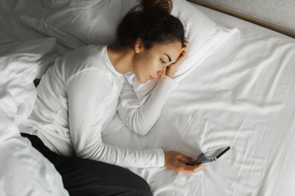 mujer en la cama, despierta mirando el móvil, sin poder dormir