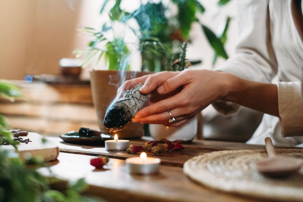 Manos de mujer quemando salvia blanca y palo santo en un antiguo ritual