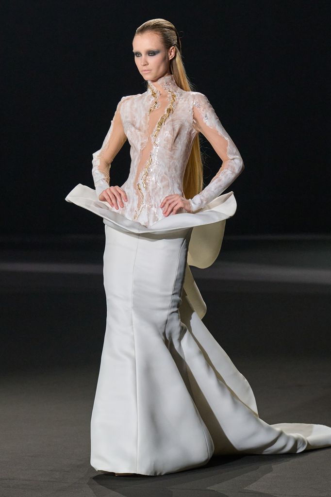 Modelo en pasarela con vestido blanco de manga larga y cola larga.
