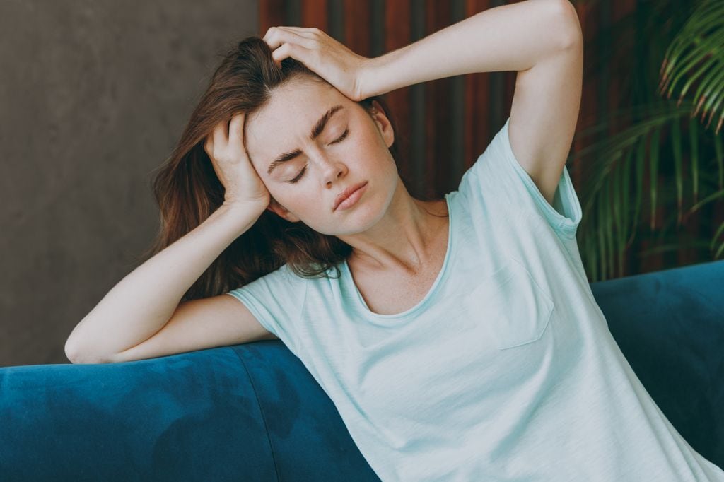 mujer con las manos en la cabeza y los ojos cerrados, con sensación de dolor