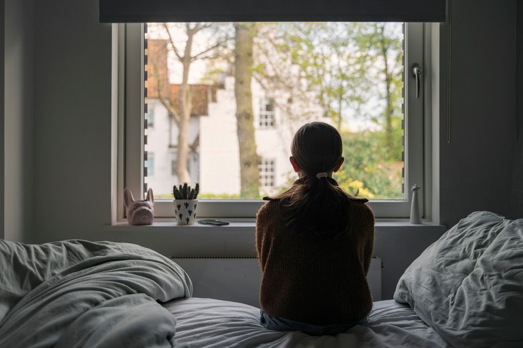 niña sentada en la cama, mirando por la ventana