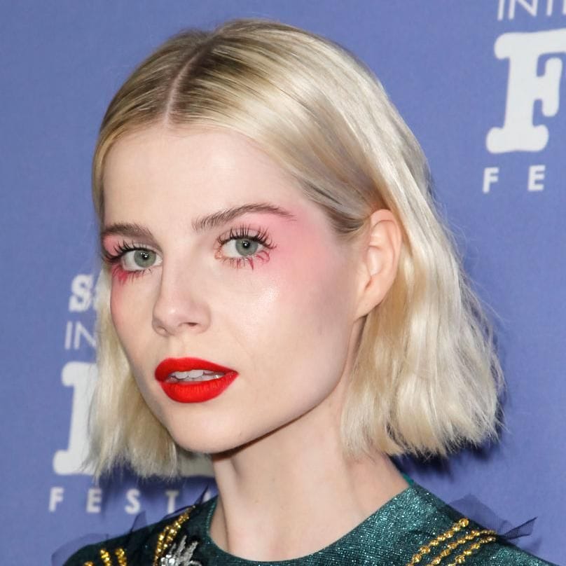 lucy boynton con maquillaje brillante en tonos rosados y rojo