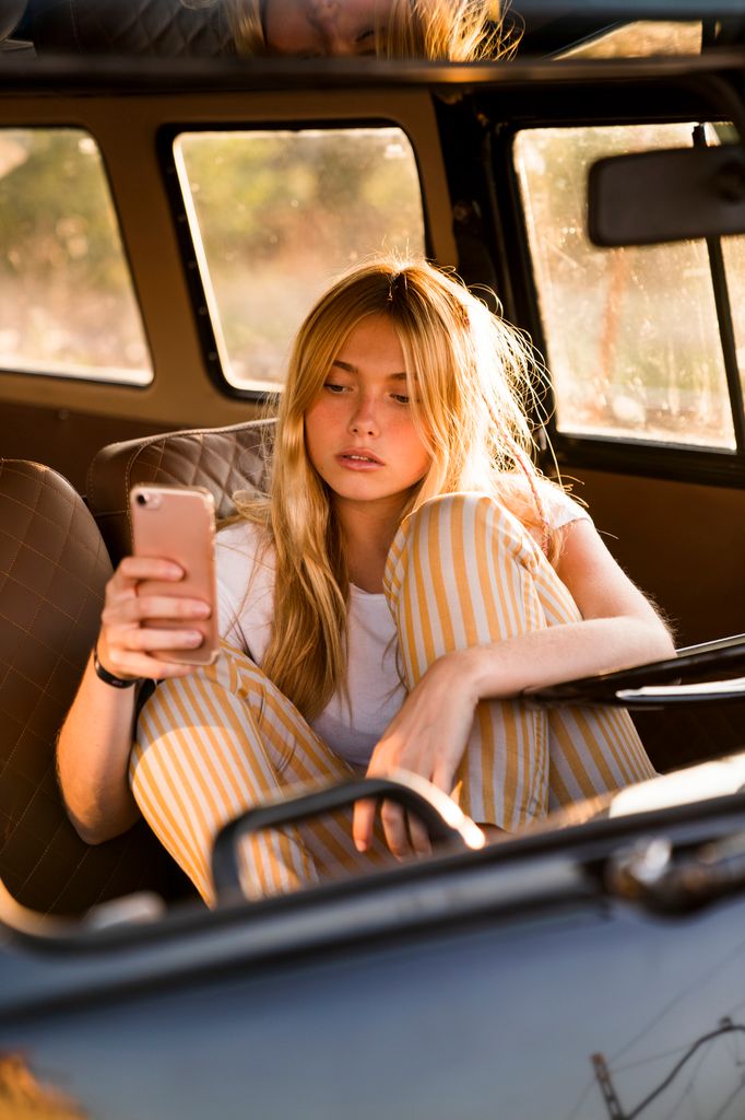 Chica joven con el móvil en el coche al sol
