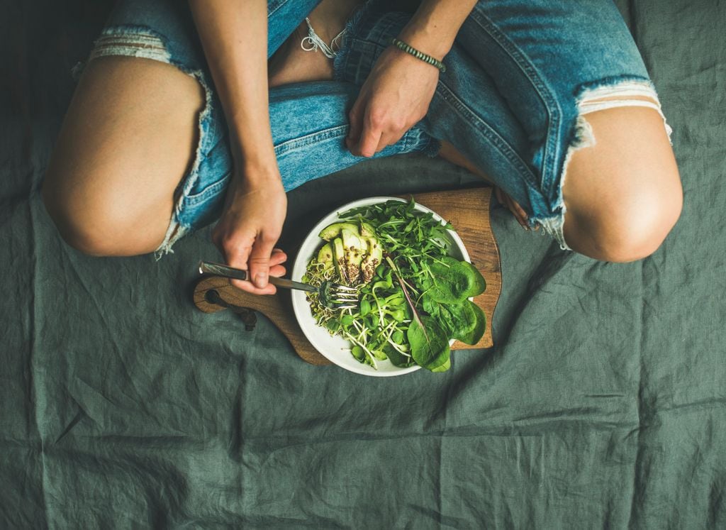 Primer plano de mujer comiendo un plato de espinacas, aguacate y brotes