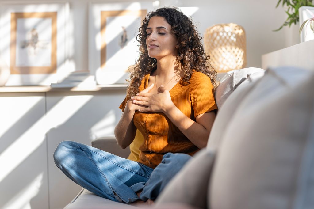 mujer joven meditando, sentada en el sofá