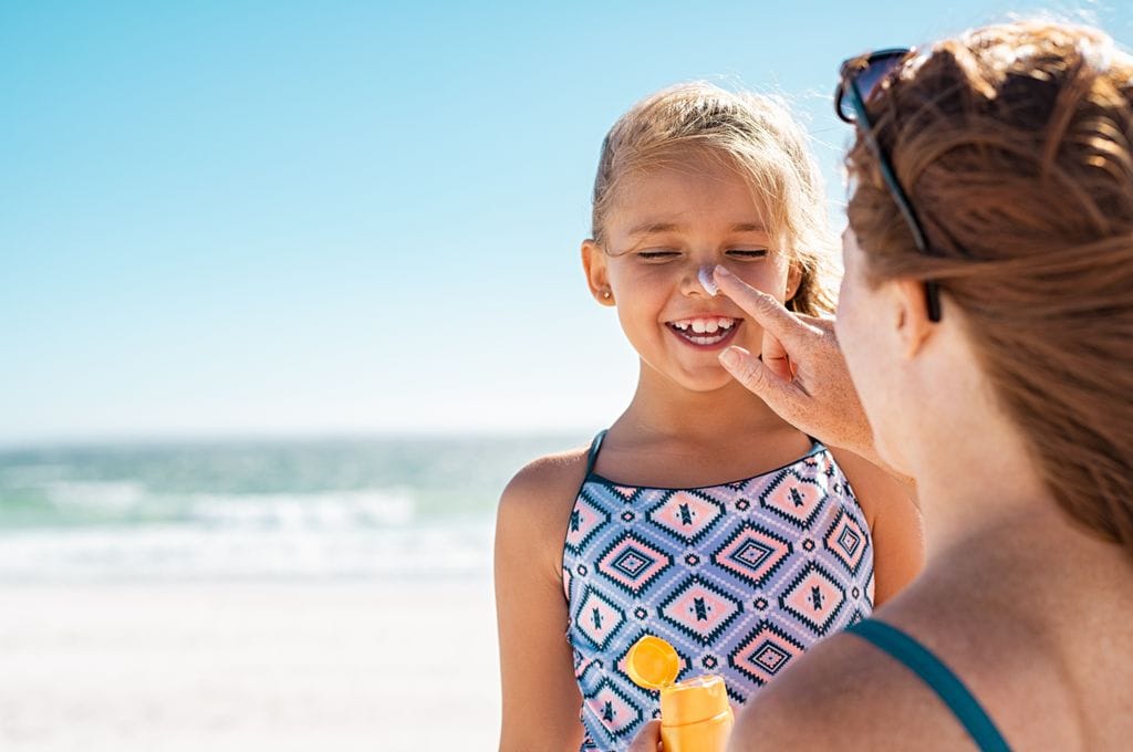 Madre aplicando crema solar a su hija en la playa