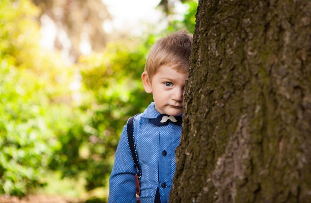 Niño tímido escondido tras un árbol