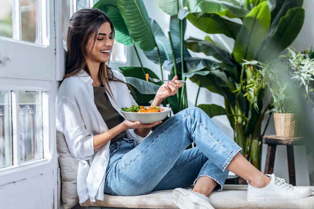 mujer feliz comiendo ensalada en el salón