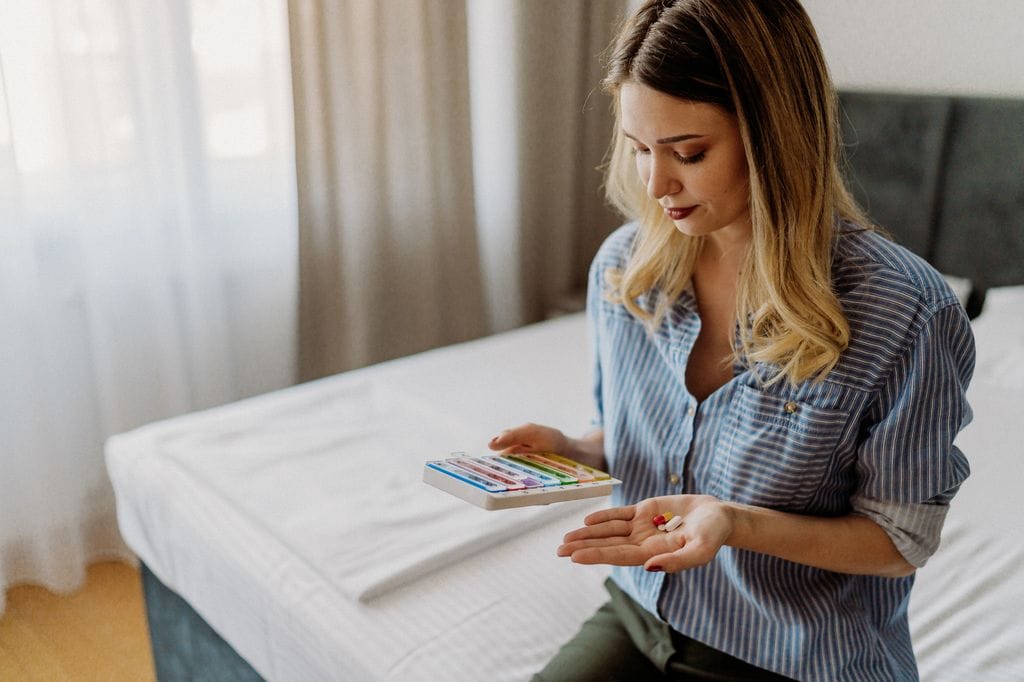 mujer mirando sus suplementos alimenticios en un pastillero