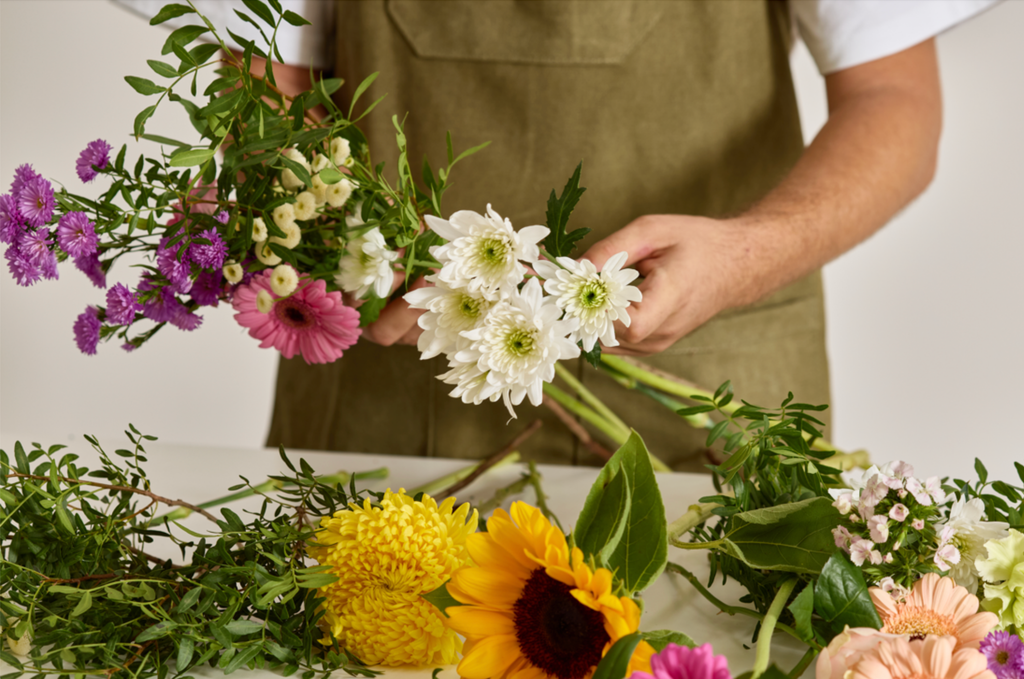Primer plano de manos trabajando en la creación de un ramo con diversas flores.