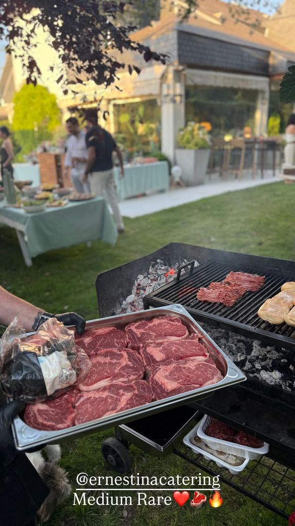 Persona con guantes negros sostiene bandeja de carne en asador al aire libre.