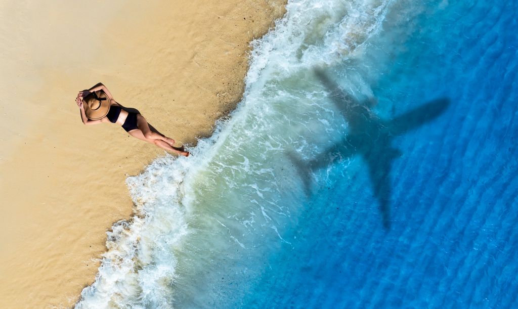 Mujer en una playa y sombra de un avión