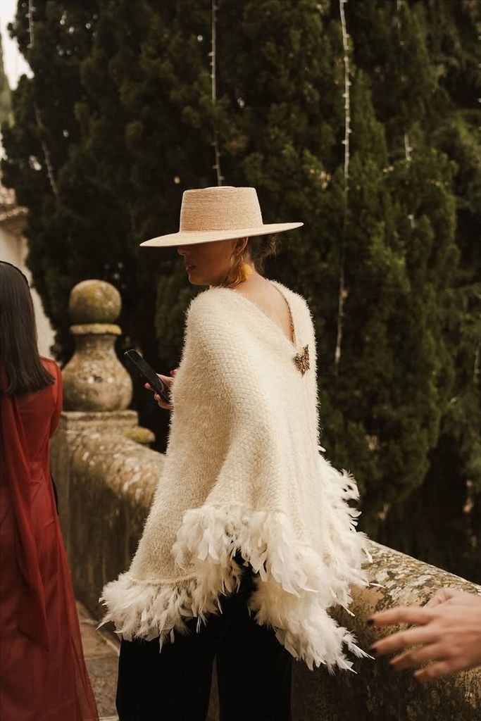 Look de invitada con poncho con aplicaciones de plumas