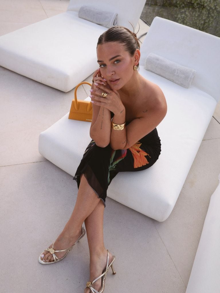 Laura Escanes con vestido negro estampado de Desigual, sandalias plateadas y bolso Jacquemus sentada