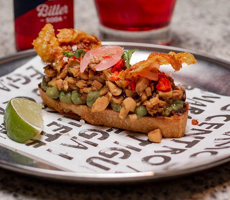 Focaccia, guacamole, pollo asado desmigado y glaseado en sus jugos, habanero asado encurtido, cebolla roja encurtida, brotes de cilantro y piel de pollo crujiente (Bar Azoka)