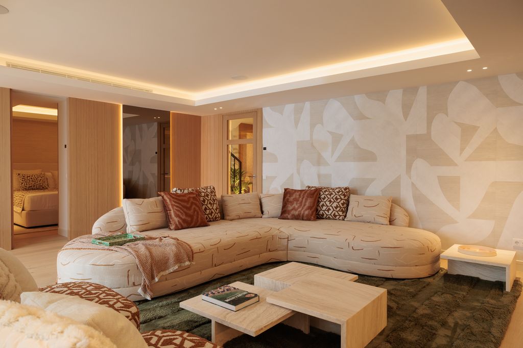 Salón con papel pintado, sofá beige, cojines en tonos tierra y beige a juego con el sofá, iluminación perimetral